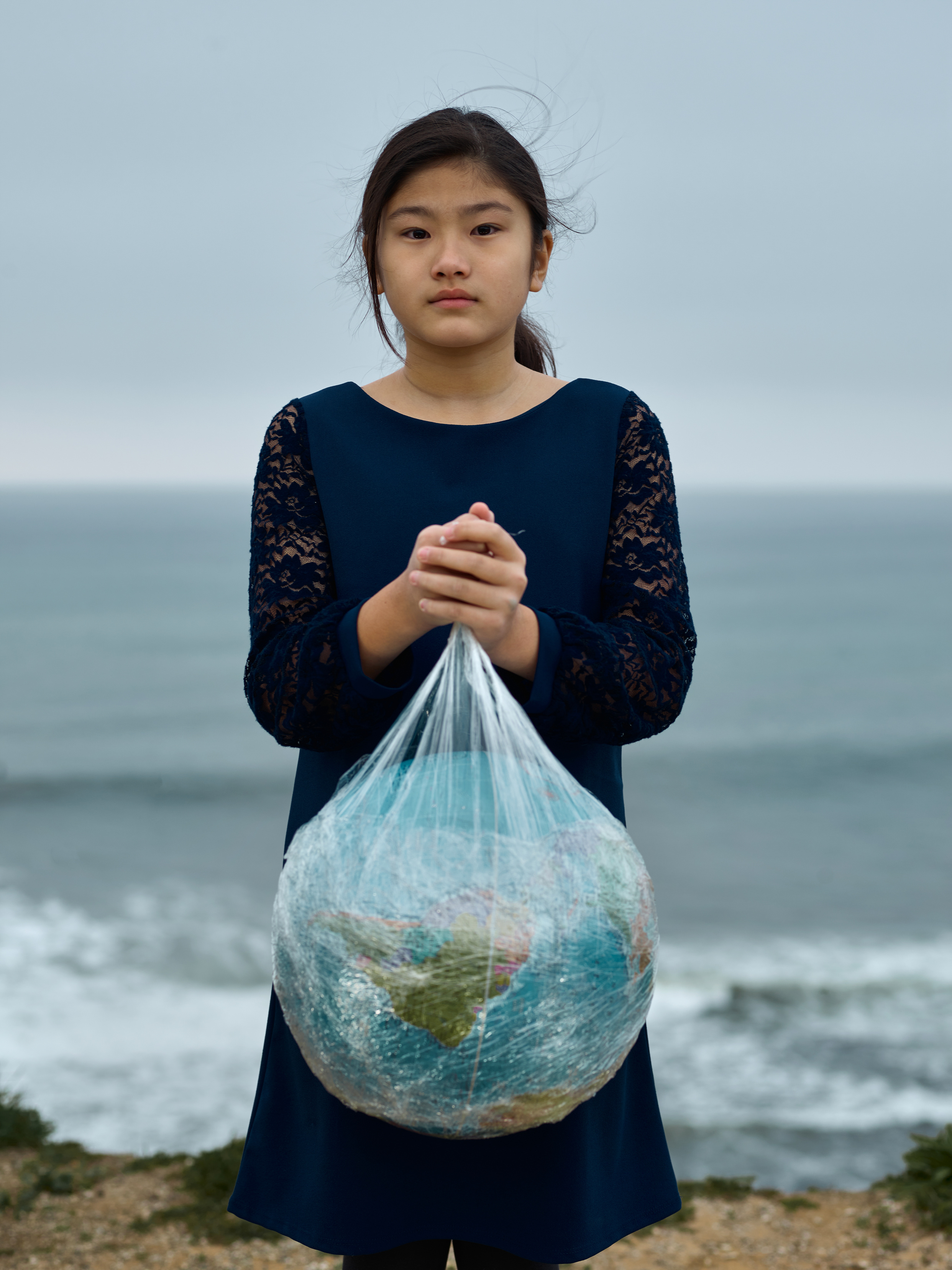 Calm girl with globe in plastic bag near seashore